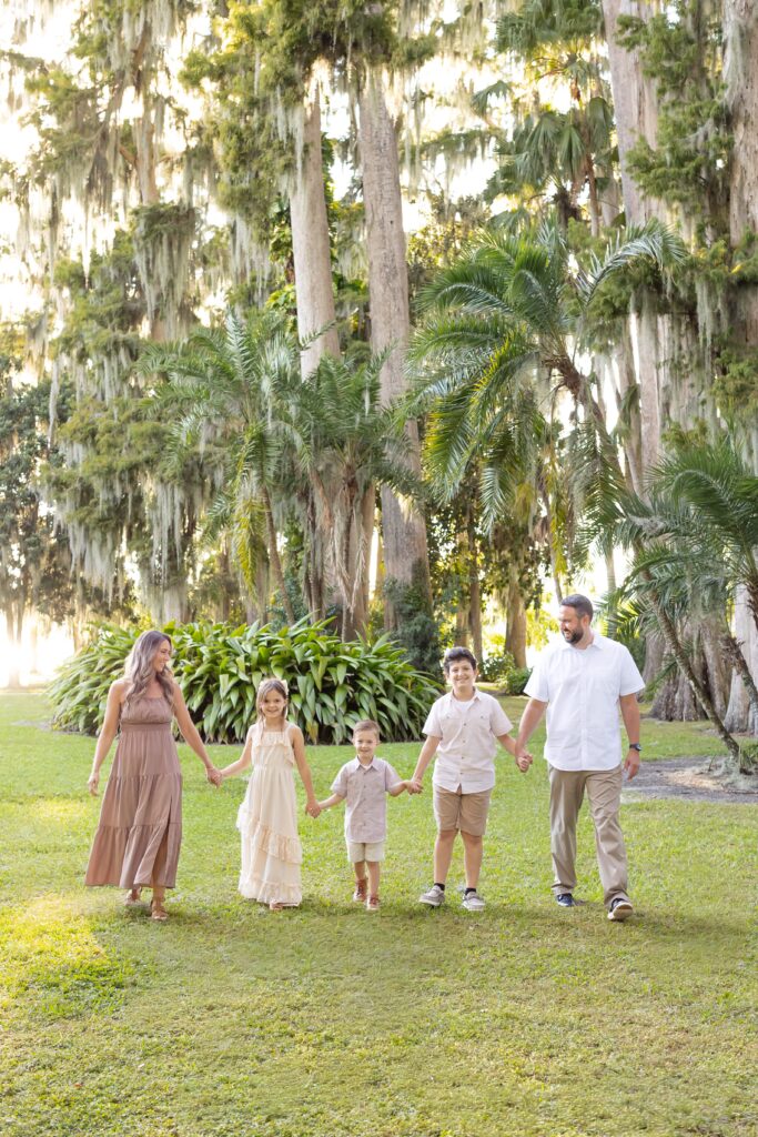Family walks and holds hands smiling at each other for their Kraft Azalea Gardens Family Photo Session in Winter Park, Florida