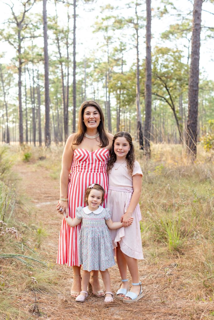 Mom holds hands with daughters in field at Wekiva Springs State Park for their family photo session
