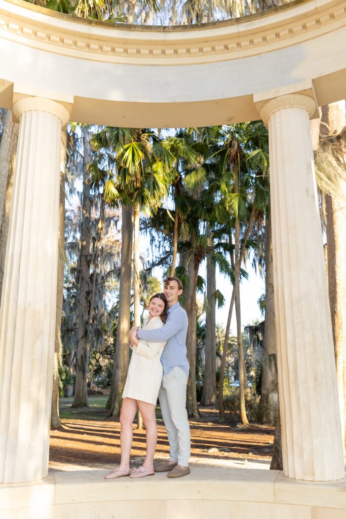 Couple cuddles on top of columns after their proposal for their engagement photos at Kraft Azalea Park in Winter Park, Florida