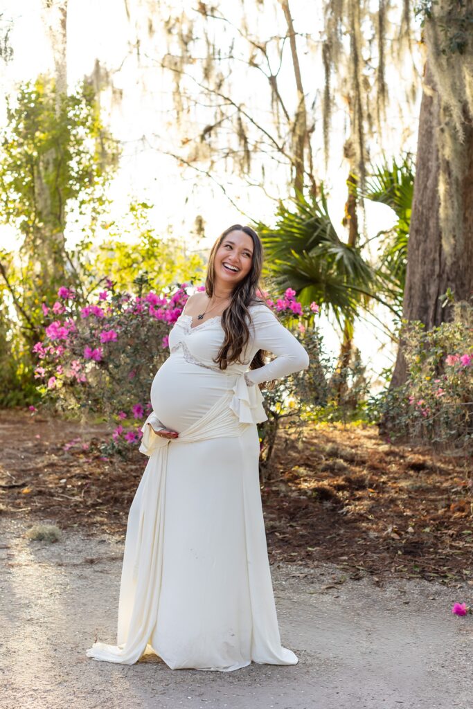 Soon to be mom holds belly and laughs for her Maternity Photography Orlando session at Kraft Azalea Garden in Winter Park, Florida